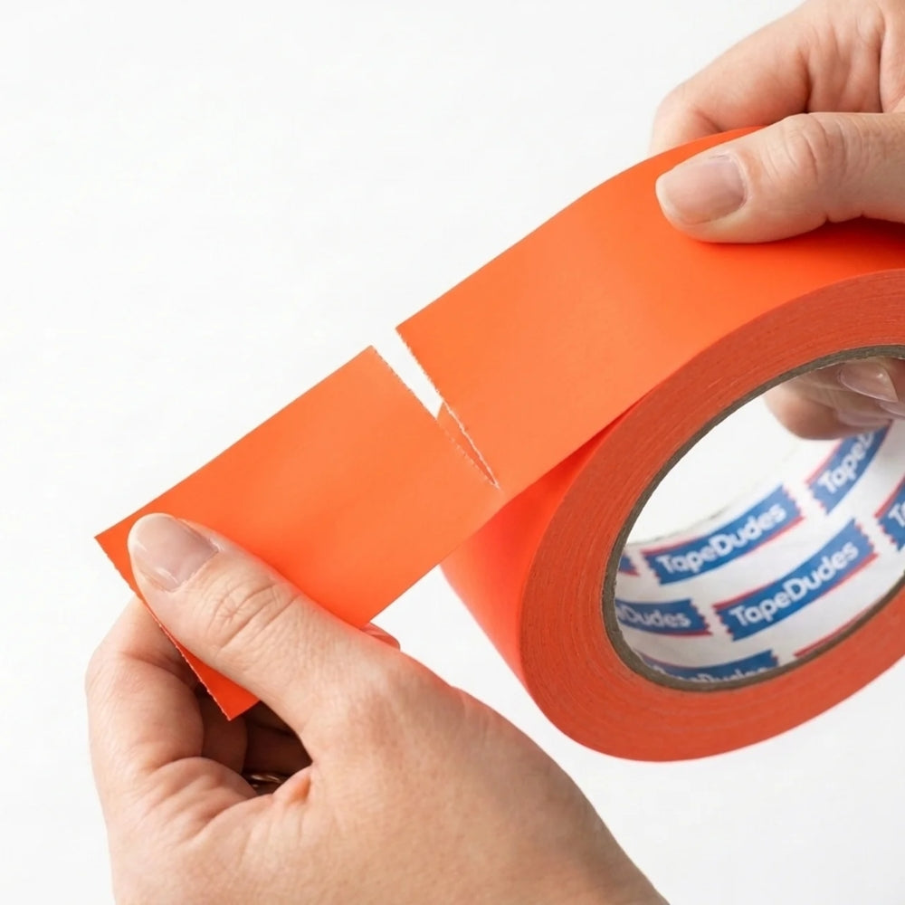Person easily tearing a strip of neon orange matte gaffer tape by tapedudes